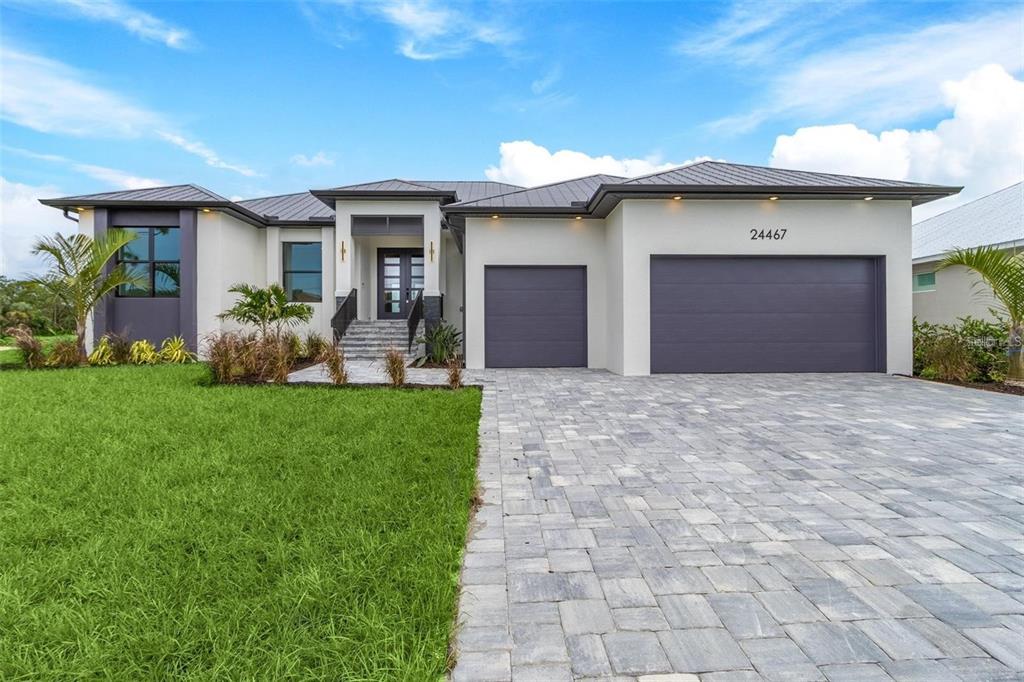 A modern single-story house features a gray metal roof, stucco exterior, and a paved driveway — 17149 SARONG LANE, PUNTA GORDA, FL