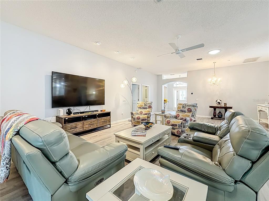A living room features light gray walls, wood-look flooring, two leather sofas, and a television — 1738 AUGUSTINE DRIVE, THE VILLAGES, FL
