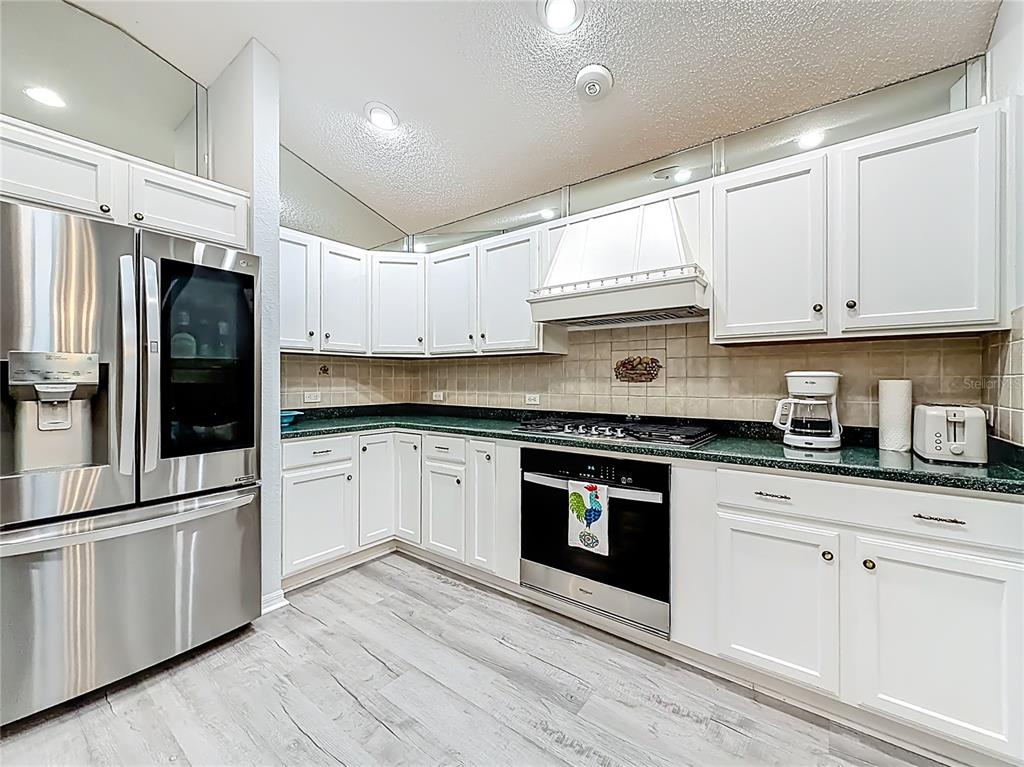 A kitchen features white cabinets, stainless steel appliances, green countertops, and light wood-look flooring — 1738 AUGUSTINE DRIVE, THE VILLAGES, FL