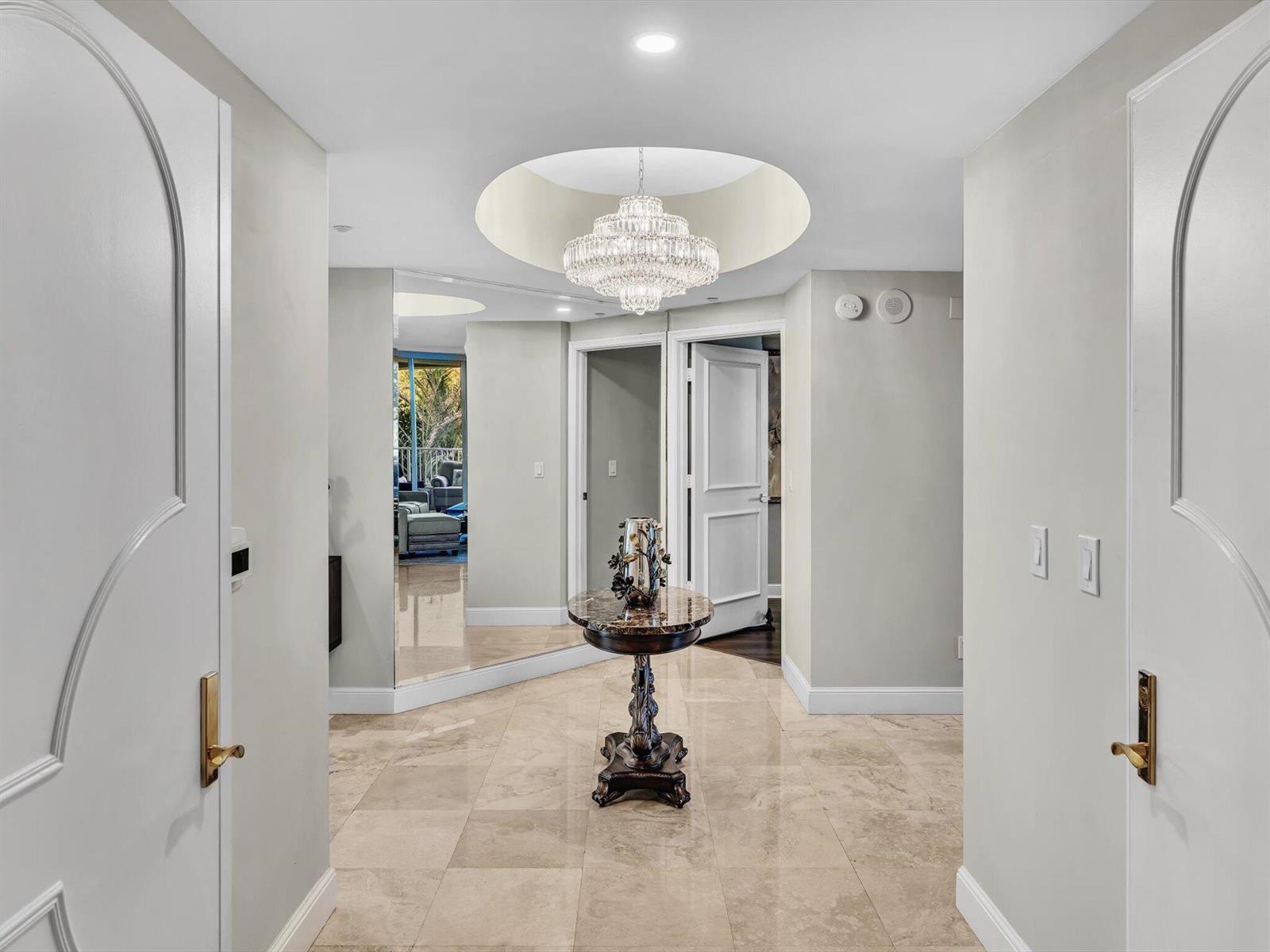 A foyer features a crystal chandelier, marble flooring, and a central pedestal table — 3720 S Ocean Boulevard # 207, Highland Beach FL 33487, HIGHLAND BEACH, FL