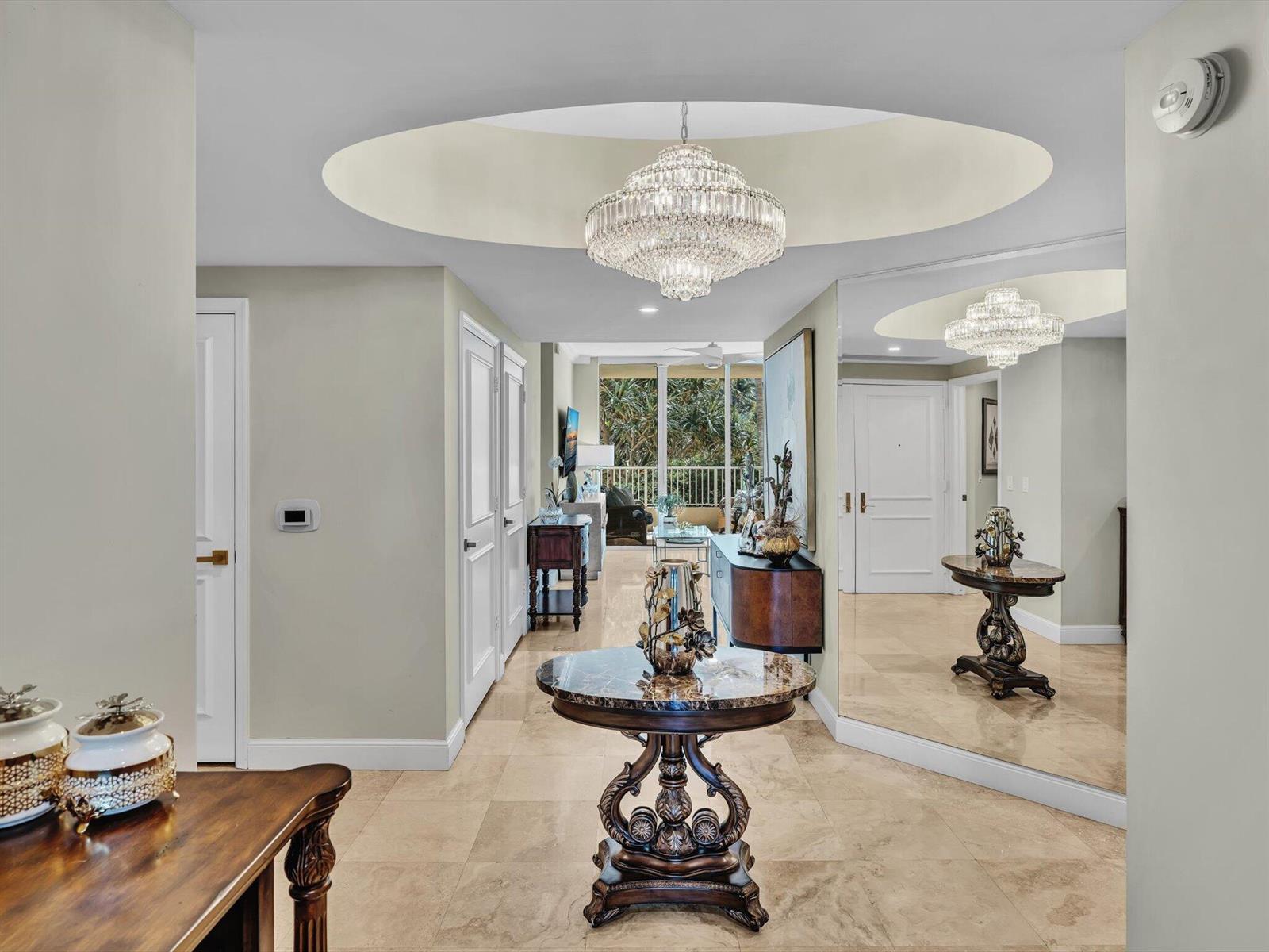 A foyer with a marble-topped pedestal table, a crystal chandelier, and a large wall mirror — 3720 S Ocean Boulevard # 207, Highland Beach FL 33487, HIGHLAND BEACH, FL