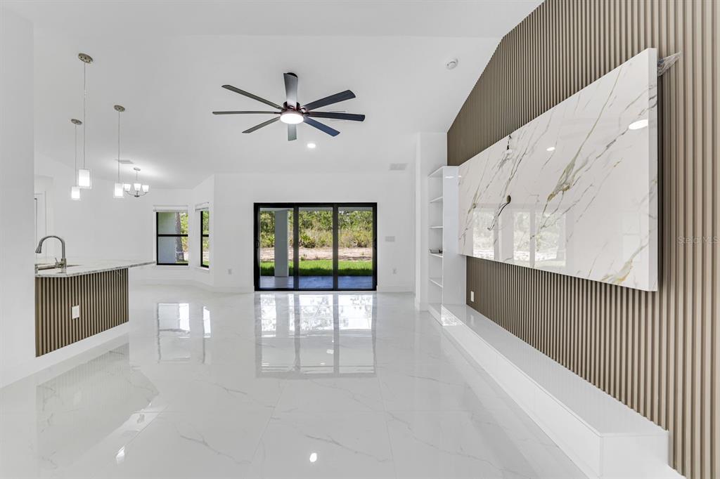 A bright living room features white tile floors, a slatted wood wall, and sliding glass doors — 3201 35TH STREET W, LEHIGH ACRES, FL