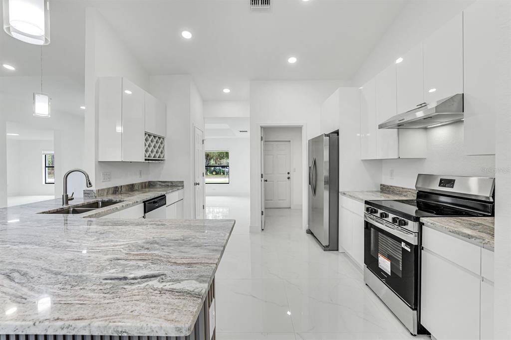 A modern kitchen features white cabinets, stainless steel appliances, and marble-patterned countertops — 3201 35TH STREET W, LEHIGH ACRES, FL