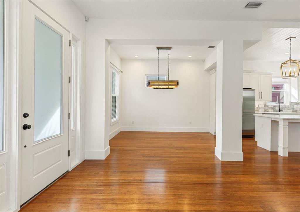 An open dining area with hardwood floors, a rectangular chandelier, and an adjacent white kitchen — 214 E FLORIBRASKA AVENUE, TAMPA, FL
