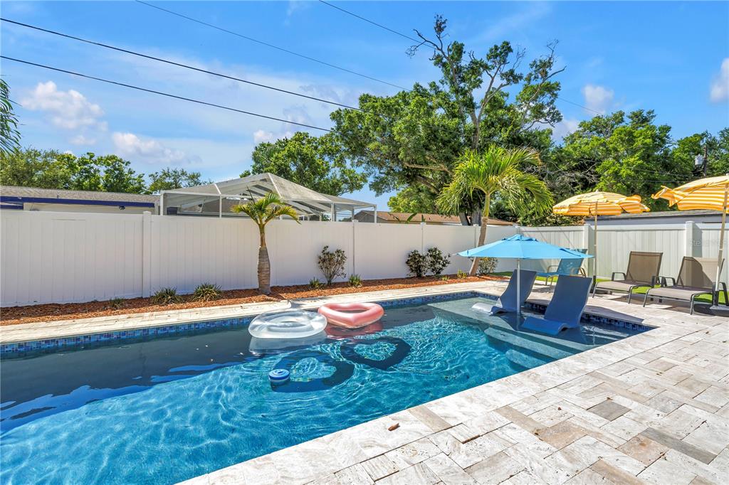 A backyard swimming pool features lounge chairs, a blue umbrella, and a white privacy fence — 12096 OAK STREET, LARGO, FL