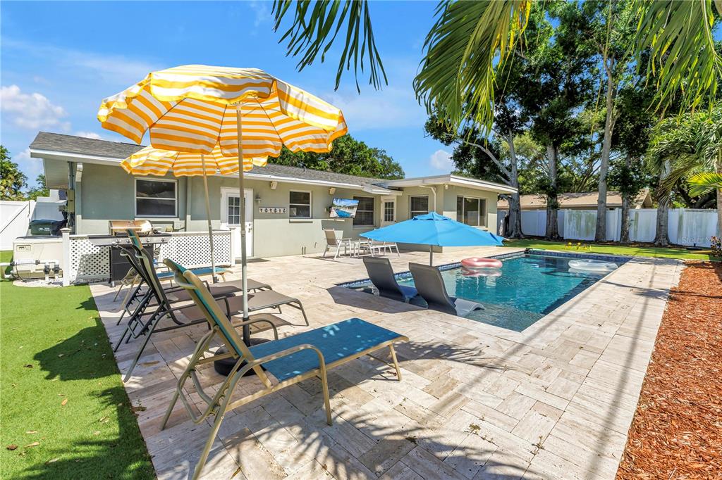 A backyard patio features a swimming pool, lounge chairs, and two umbrellas near a house — 12096 OAK STREET, LARGO, FL