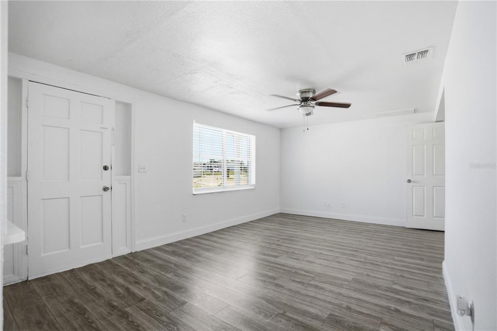 An empty room with white walls, gray wood-look flooring, a ceiling fan, and white doors — 3301 ROSEFIELD DRIVE, HOLIDAY, FL