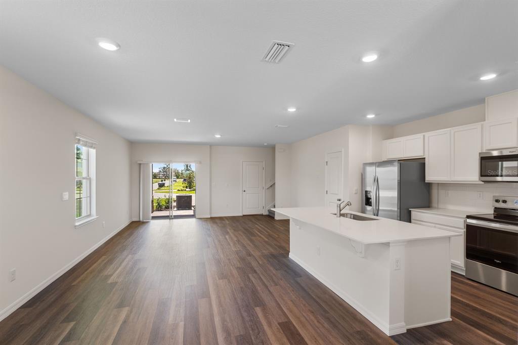 An open-concept kitchen and living area with white cabinets, a central island, and wood flooring — 16503 BARBOURS CREEK WAY, WINTER GARDEN, FL