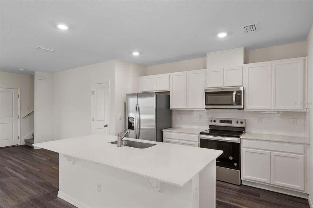 A modern kitchen features white cabinets, stainless steel appliances, and a large quartz-topped island — 16503 BARBOURS CREEK WAY, WINTER GARDEN, FL