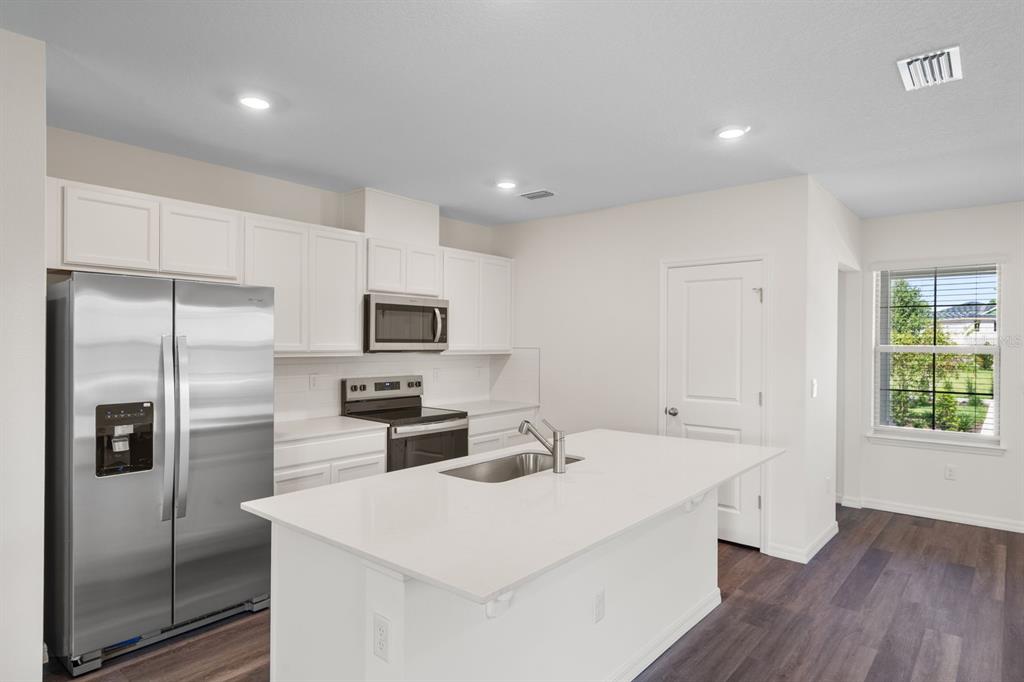 A kitchen features white cabinets, stainless steel appliances, a center island, and dark wood flooring — 16503 BARBOURS CREEK WAY, WINTER GARDEN, FL