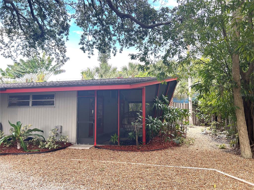 A single-story house with a gravel driveway, red trim, and mature trees in the yard — 4830 HIGEL AVENUE, SARASOTA, FL