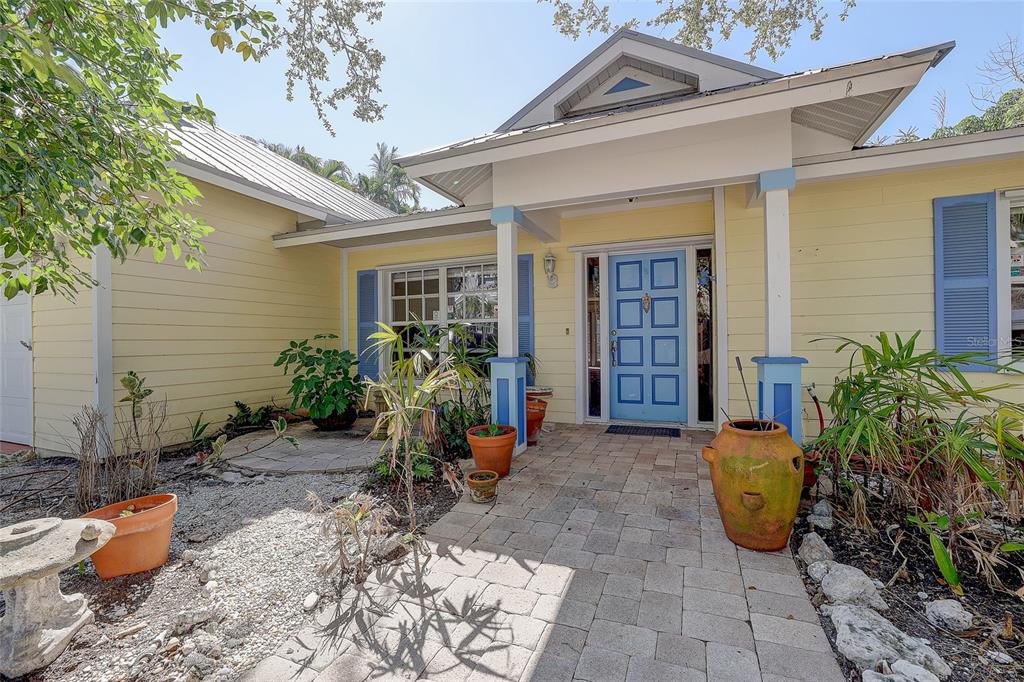 A yellow house exterior features a blue front door, a stone walkway, and potted plants — 226 OGDEN STREET, SARASOTA, FL