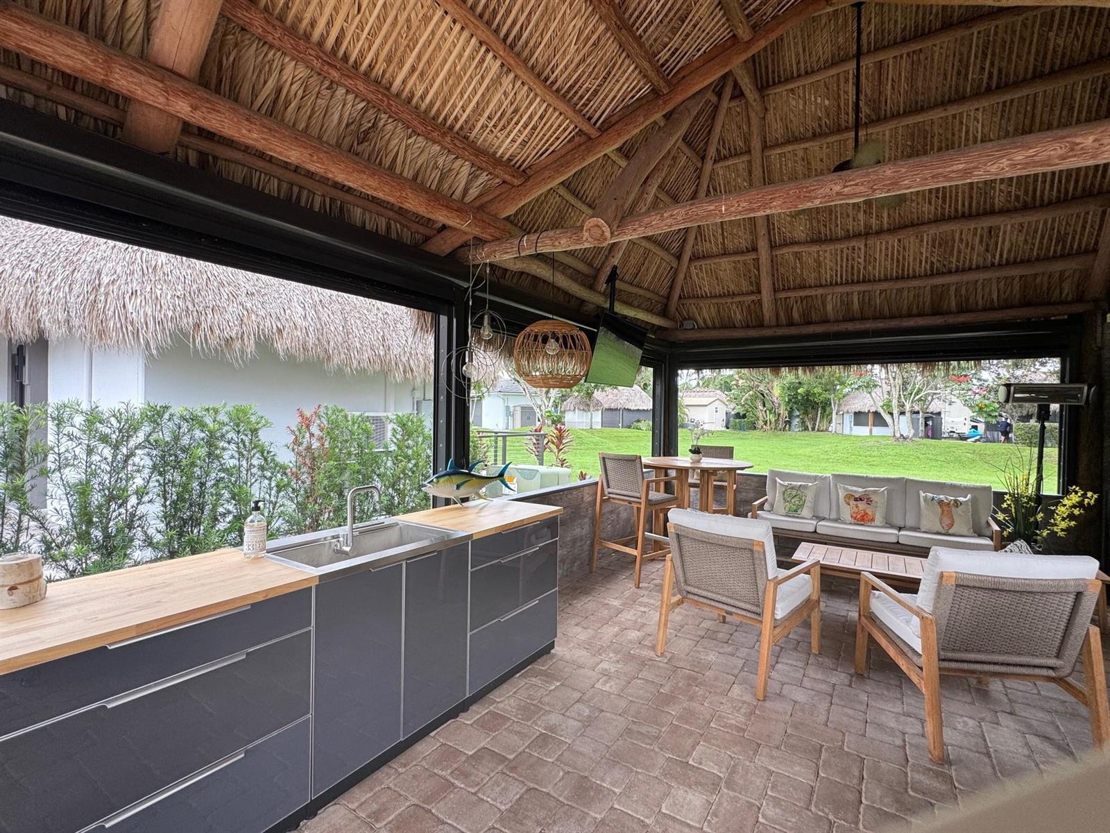 An outdoor kitchen and lounge area under a thatched roof with grey cabinets and seating — 373 Sundial Circle # 373, Margate FL 33068, MARGATE, FL