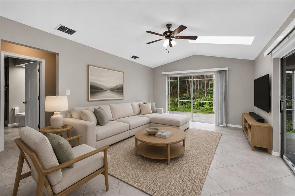 A living room with a sectional sofa, round coffee table, ceiling fan, and sliding glass doors — 9504 VIA SEGOVIA, NEW PORT RICHEY, FL