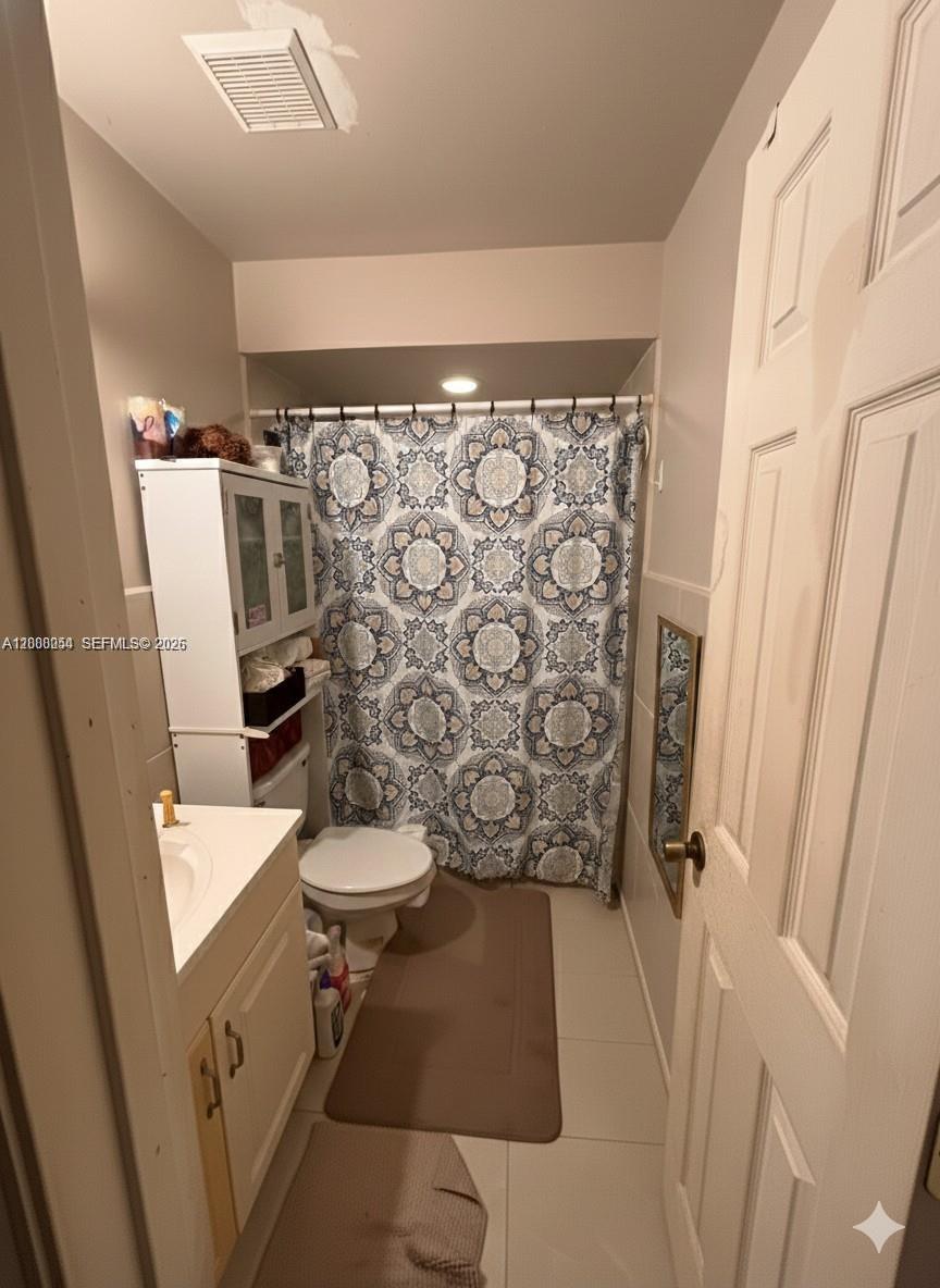 A small bathroom features a white vanity, a toilet, and a patterned shower curtain — 1415 NW 80th Ave # D, Margate FL 33063, MARGATE, FL