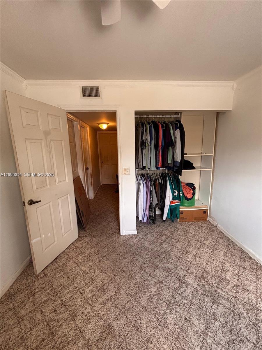 A bedroom features a carpeted floor, an open closet with hanging clothes, and an adjacent hallway — 1415 NW 80th Ave # D, Margate FL 33063, MARGATE, FL