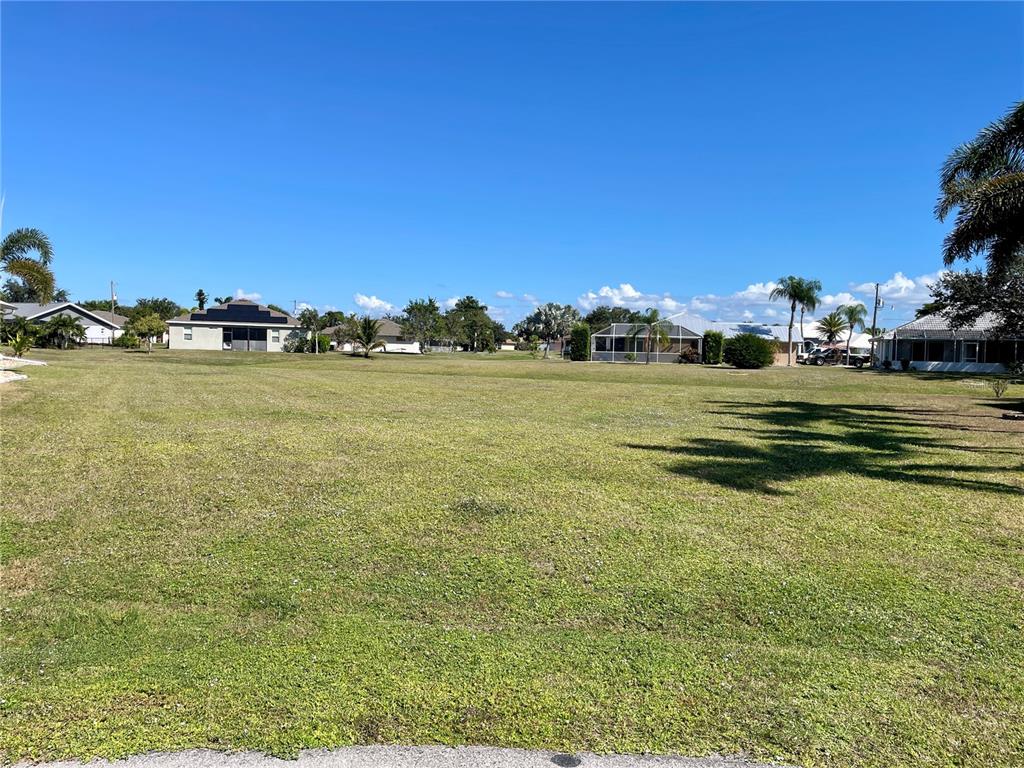 A wide, grassy vacant lot is surrounded by residential houses under a clear blue sky — 7310 SATSUMA DRIVE, PUNTA GORDA, FL