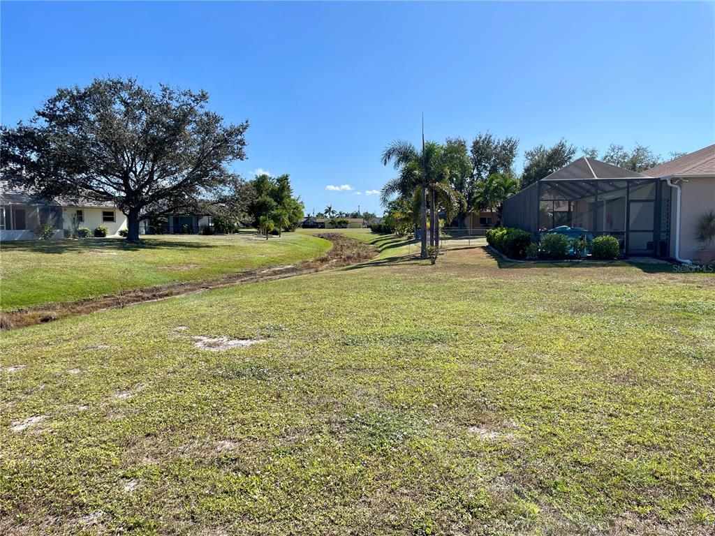 A grassy backyard features a small drainage ditch, palm trees, and a screened-in patio — 7310 SATSUMA DRIVE, PUNTA GORDA, FL