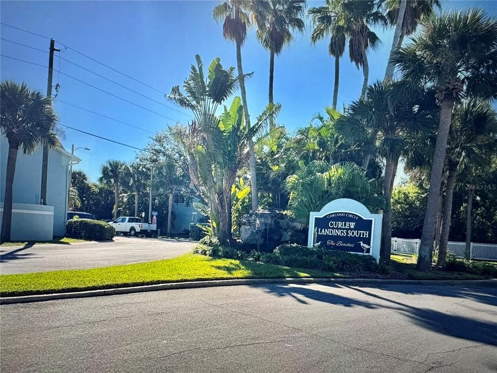 A sign for Curlew Landings South stands near palm trees and a paved entrance road — 629 GARLAND CIRCLE, INDIAN ROCKS BEACH, FL