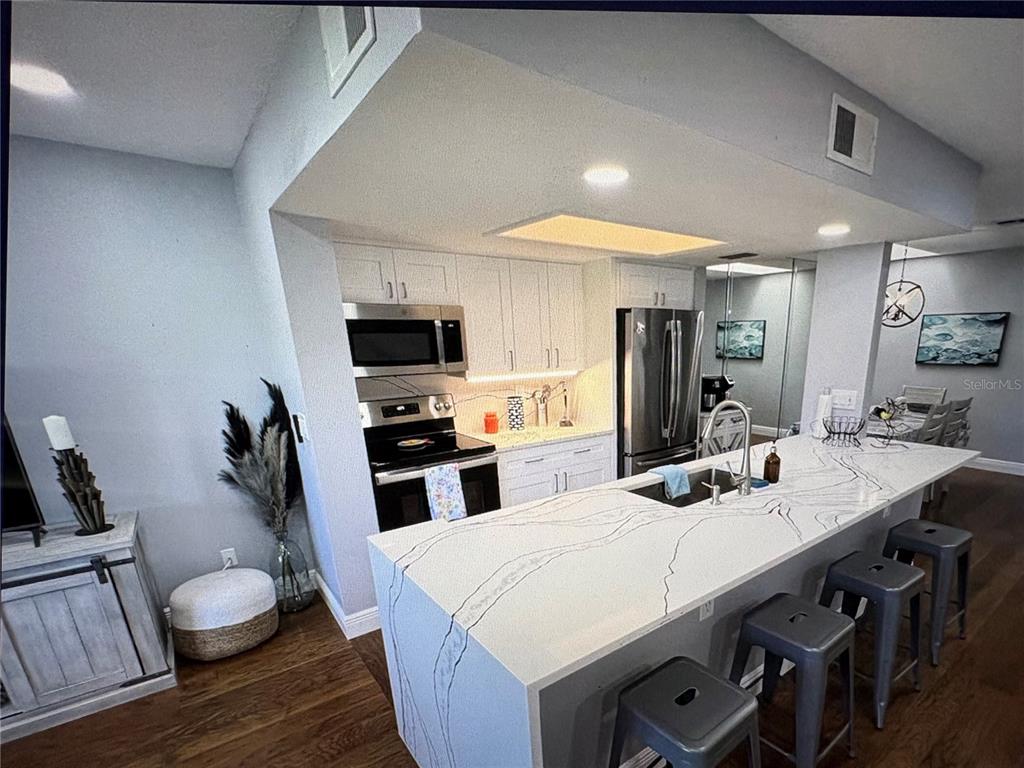 A kitchen features white cabinets, stainless steel appliances, and a large waterfall-edge quartz island — 629 GARLAND CIRCLE, INDIAN ROCKS BEACH, FL