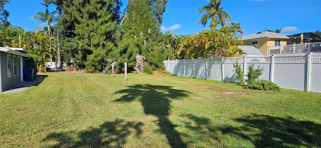A grassy backyard features a white vinyl fence, palm trees, and a neighboring house — TENNESSEE AVENUE, CRYSTAL BEACH, FL