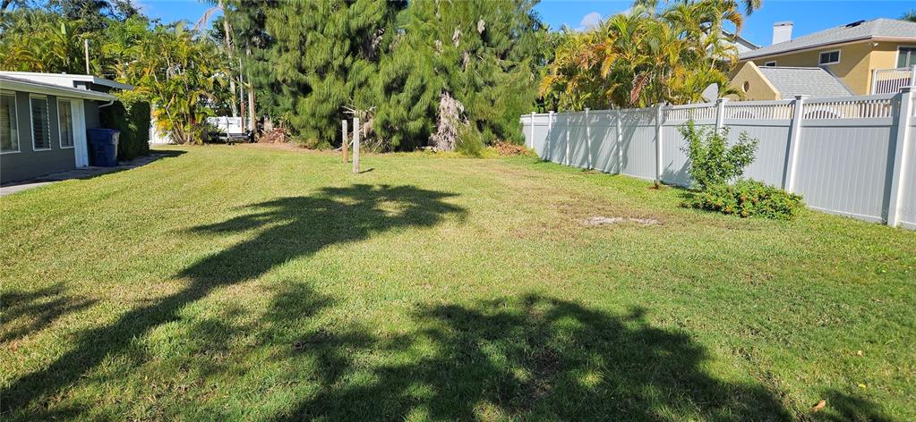 A grassy backyard features a white vinyl fence, mature trees, and a side of a house — TENNESSEE AVENUE, CRYSTAL BEACH, FL