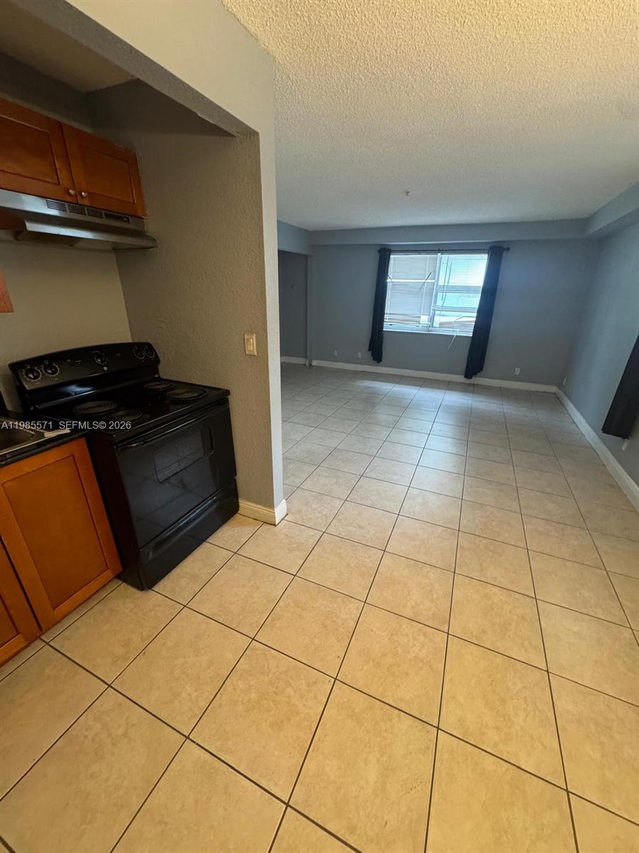 A kitchen with wooden cabinets and a black stove overlooks a tiled living area — 4251 NW 5th St # 106, Plantation FL 33317, PLANTATION, FL