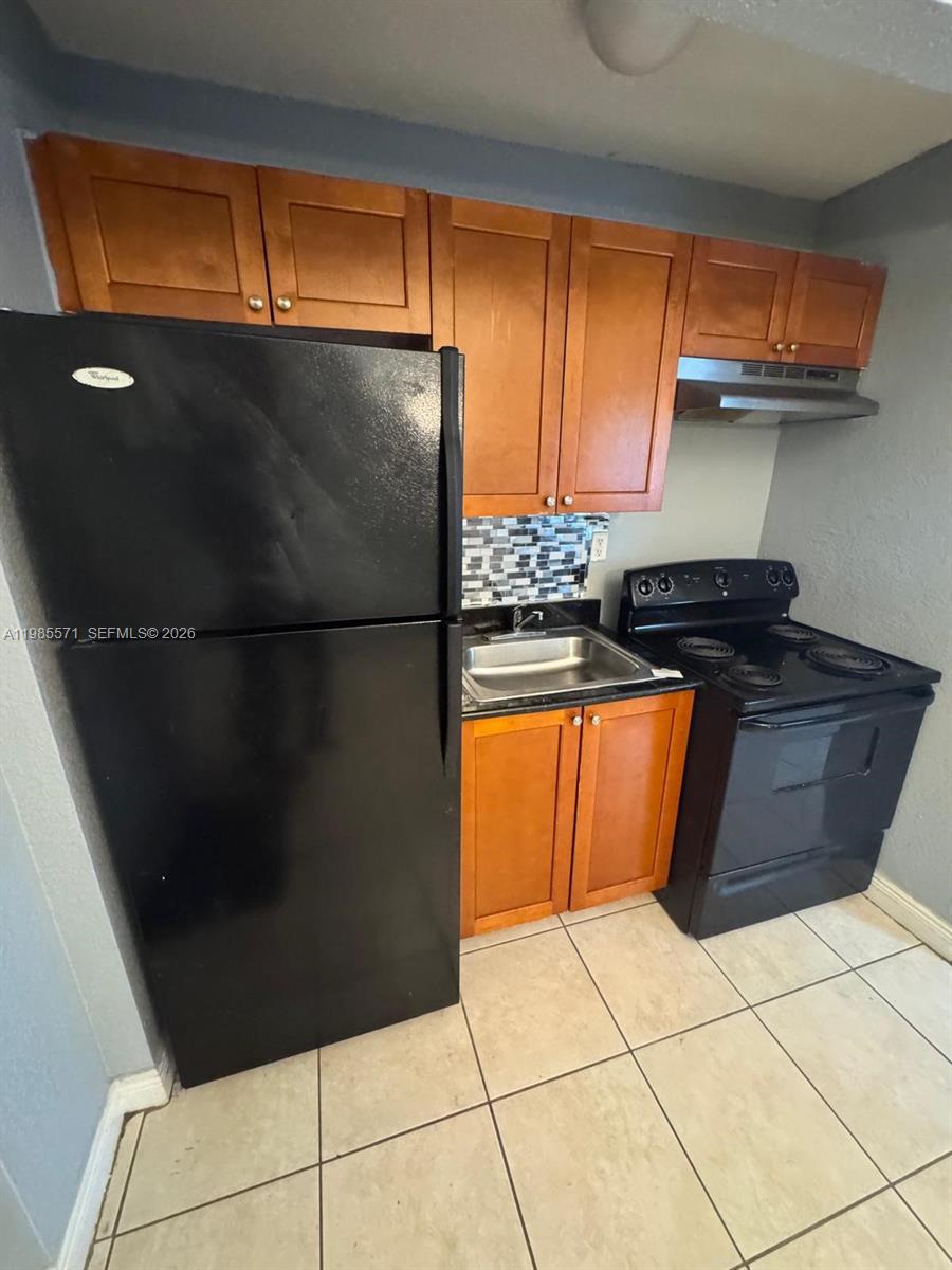 A small kitchen features black appliances, wooden cabinets, a tiled backsplash, and light floor tiles — 4251 NW 5th St # 106, Plantation FL 33317, PLANTATION, FL