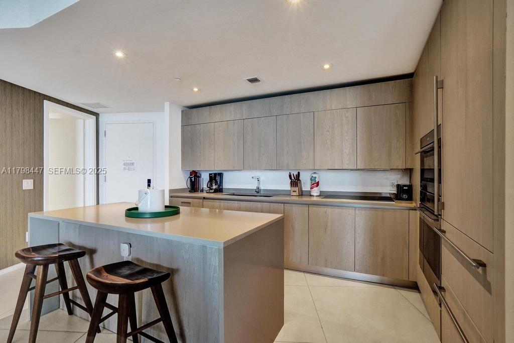 A modern kitchen features light wood cabinetry, a central island with bar stools, and stainless appliances — 4111 S Ocean Dr # 2803, Hollywood FL 33019, HOLLYWOOD, FL