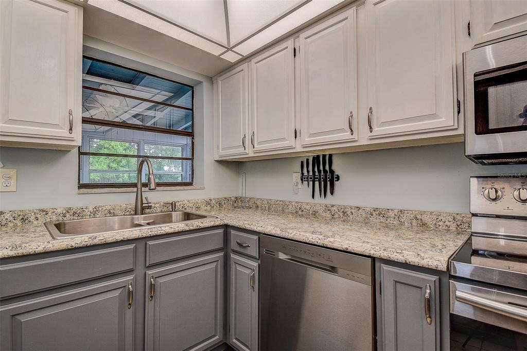A kitchen features white upper cabinets, gray lower cabinets, granite countertops, and stainless steel appliances — 6237 DALTON STREET, SPRING HILL, FL