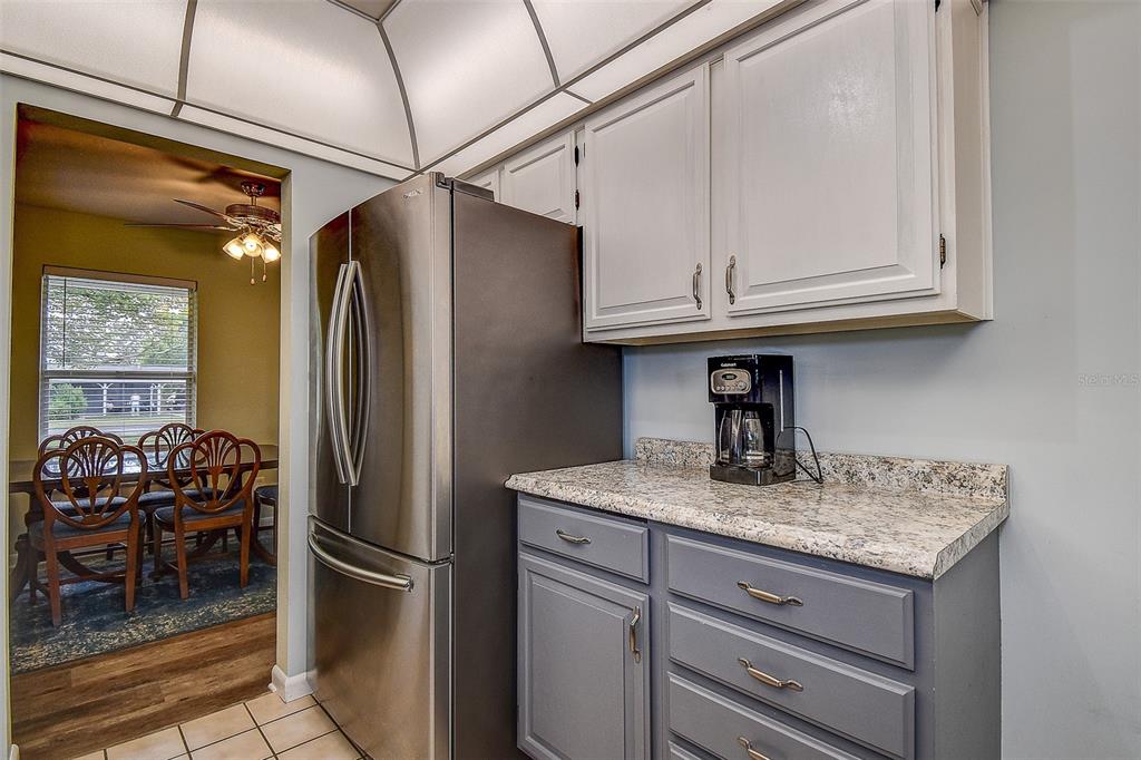 A kitchen features gray lower cabinets, white upper cabinets, granite countertops, and a stainless refrigerator — 6237 DALTON STREET, SPRING HILL, FL