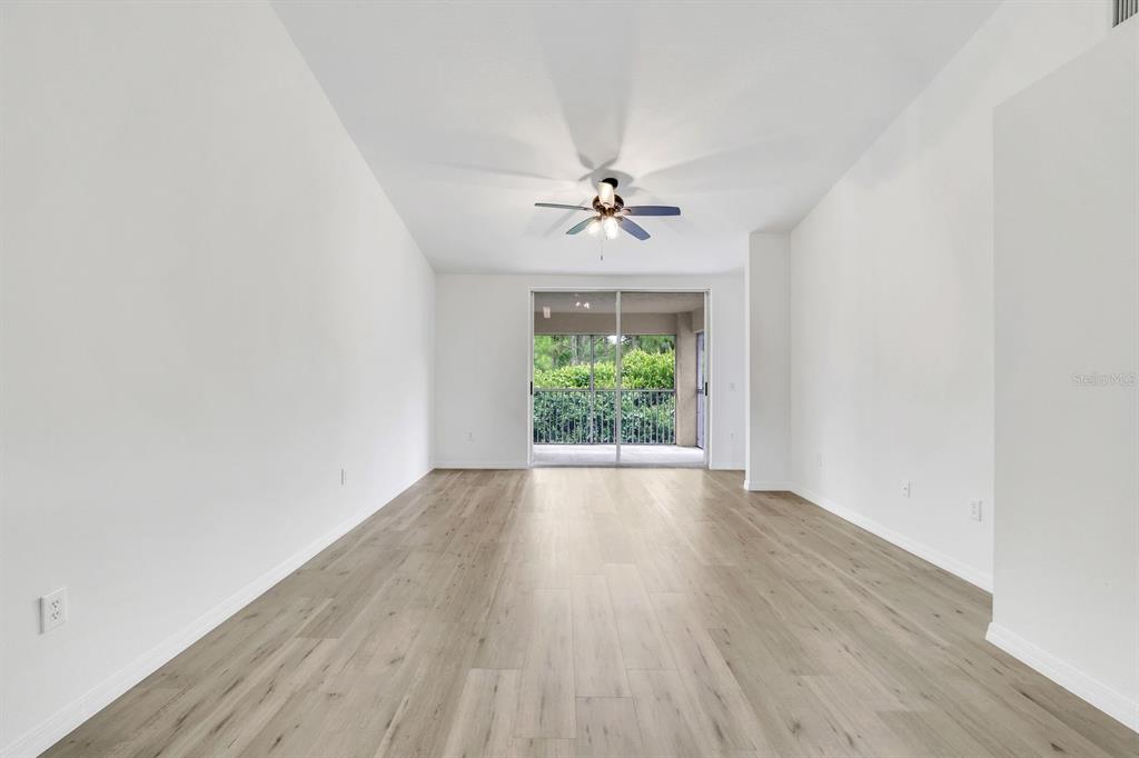 An empty living room with light wood-look flooring, white walls, and a sliding glass door — 6635 HUNTINGTON LAKES CIRCLE UNIT 202, NAPLES, FL