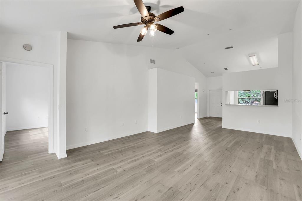 An empty living room features vaulted ceilings, a ceiling fan, and light wood-look flooring — 6635 HUNTINGTON LAKES CIRCLE UNIT 202, NAPLES, FL