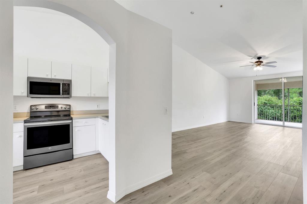 A kitchen with white cabinets and stainless steel appliances opens into a bright living area — 6635 HUNTINGTON LAKES CIRCLE UNIT 202, NAPLES, FL