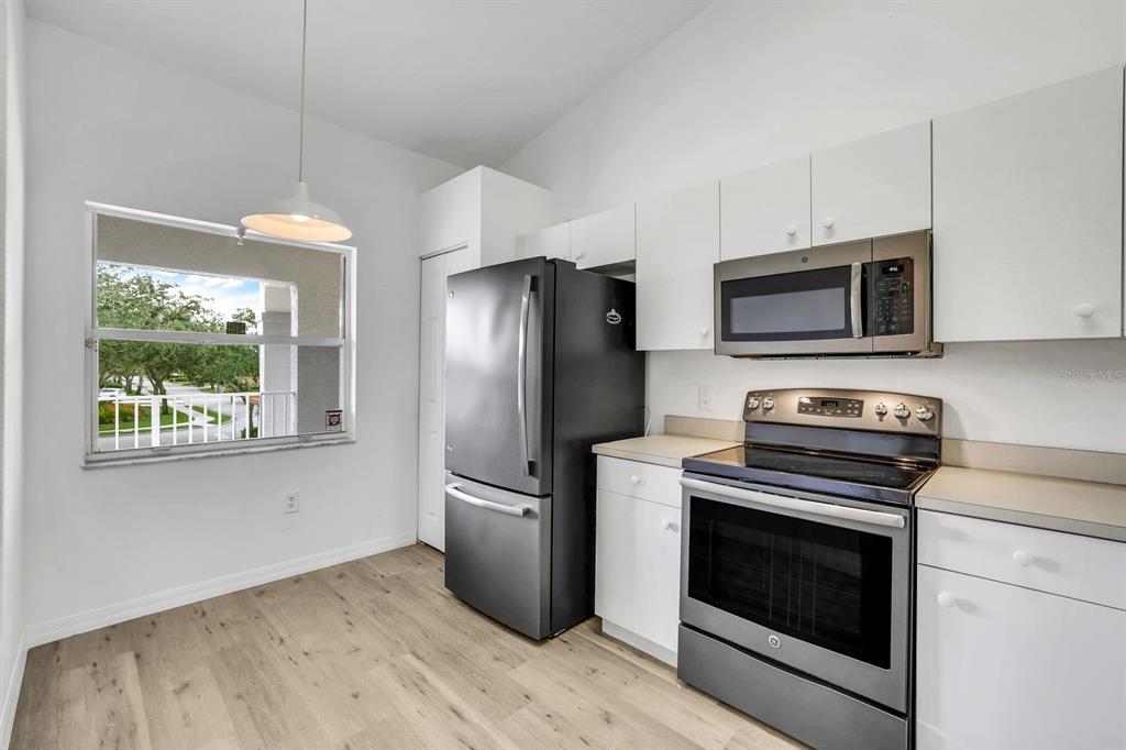 A kitchen features white cabinets, stainless steel appliances, a black refrigerator, and a window view — 6635 HUNTINGTON LAKES CIRCLE UNIT 202, NAPLES, FL