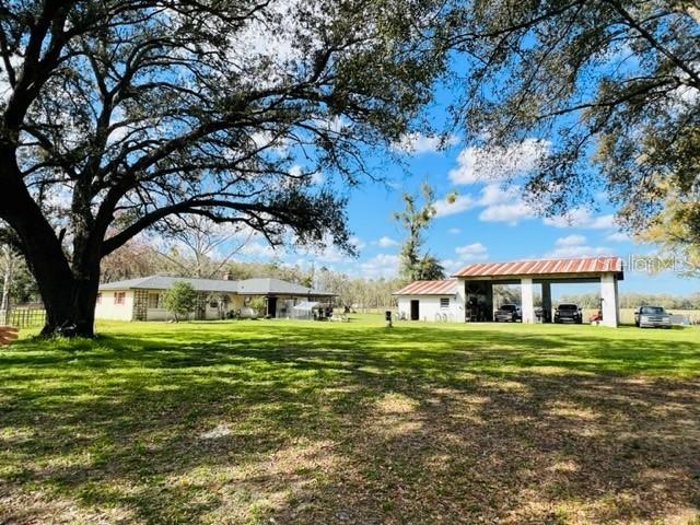A house and a detached open-air garage sit on a grassy lot with large trees — 10 SW 50TH AVENUE, BELL, FL