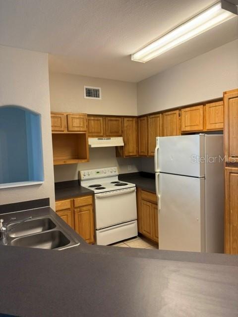 A kitchen features wood cabinets, white appliances, and a dark countertop — 3250 CORONA VILLAGE WAY UNIT 108, ORLANDO, FL