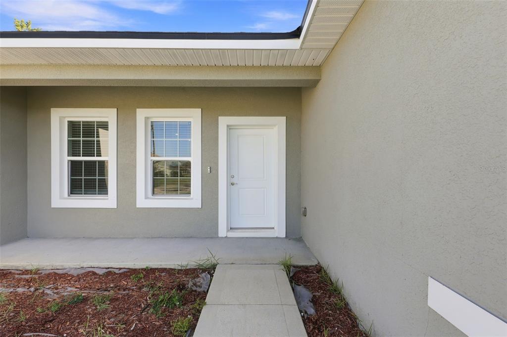 A concrete walkway leads to the front entrance of a house with two windows — 304 BEGONIA COURT, POINCIANA, FL