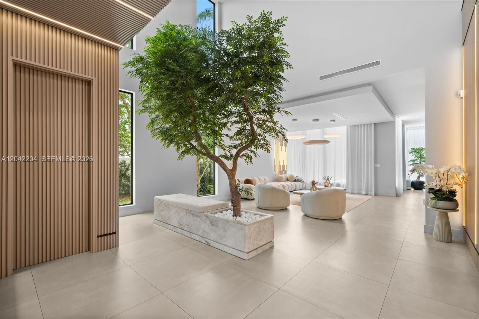 A modern, open-concept living room features a large indoor tree in a stone planter — 6814 NW 104th Ct, Doral FL 33178, DORAL, FL