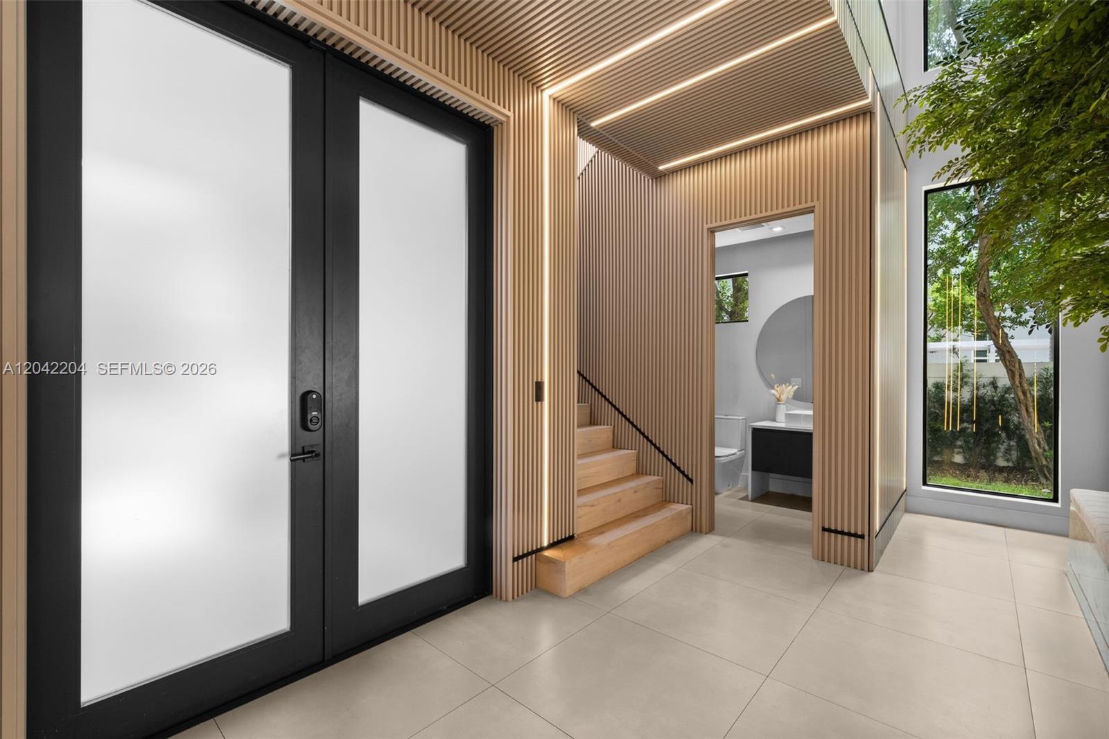 A modern entryway features wood-slatted walls, a staircase, a glass door, and a small bathroom — 6814 NW 104th Ct, Doral FL 33178, DORAL, FL