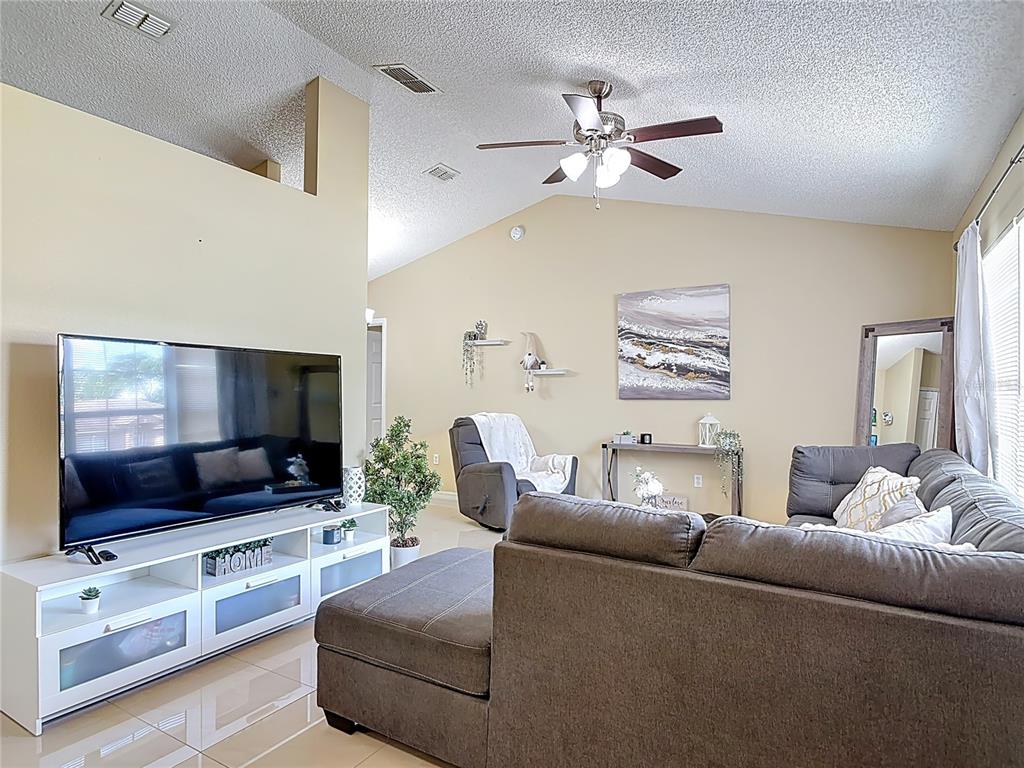 A living room features a vaulted ceiling, a ceiling fan, a sectional sofa, and a television — 1618 AIRMONT AVENUE, DELTONA, FL