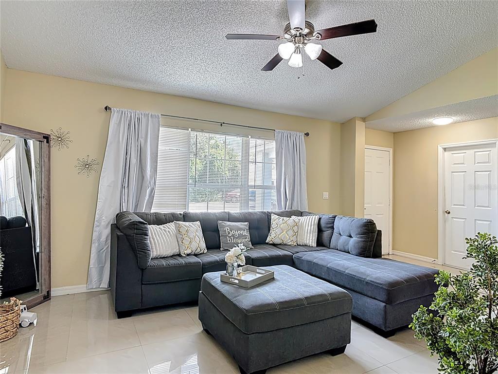 A living room features a large gray sectional sofa, a matching ottoman, and a ceiling fan — 1618 AIRMONT AVENUE, DELTONA, FL