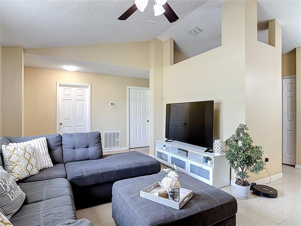 A living room features a gray sectional sofa, a television on a white stand, and tile flooring — 1618 AIRMONT AVENUE, DELTONA, FL