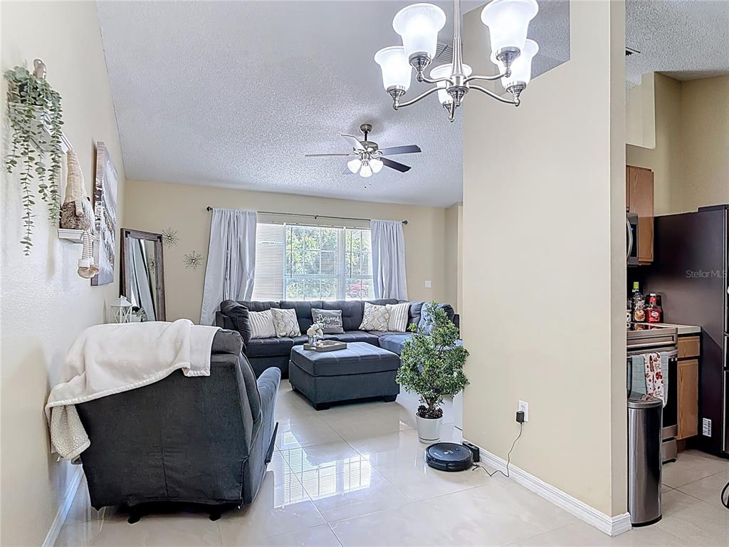 A living room with a gray sectional, tile flooring, and an adjacent kitchen area — 1618 AIRMONT AVENUE, DELTONA, FL