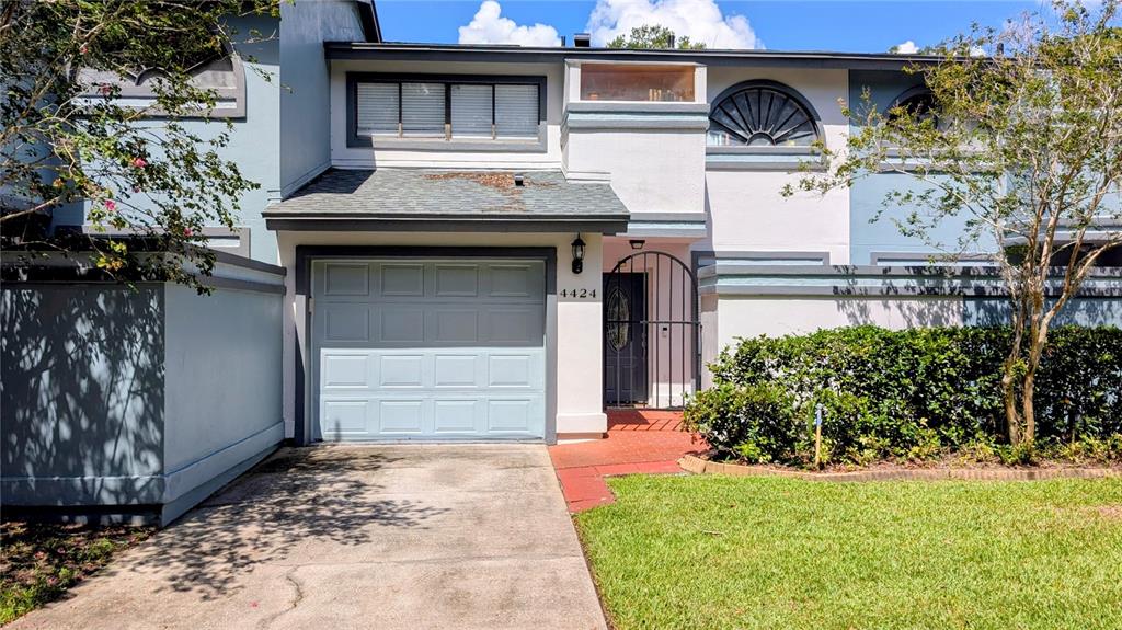 A two-story townhouse features a single-car garage, a gated entryway, and a small front lawn — 4424 DUNWOODY PLACE UNIT 13, ORLANDO, FL
