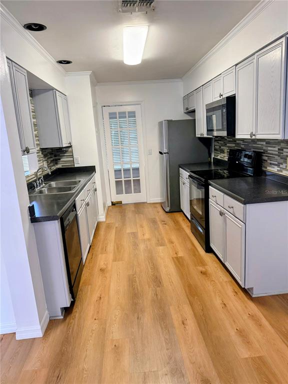 A galley kitchen features light gray cabinets, dark countertops, stainless steel appliances, and wood-look flooring — 4424 DUNWOODY PLACE UNIT 13, ORLANDO, FL
