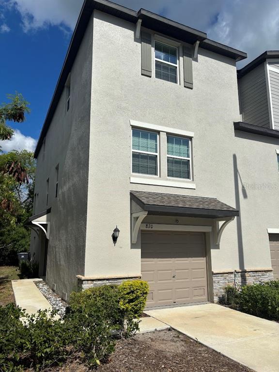 A three-story townhouse exterior features a tan stucco facade, a single-car garage, and stone accents — 870 TENNYSON MILL CIRCLE, TAMPA, FL