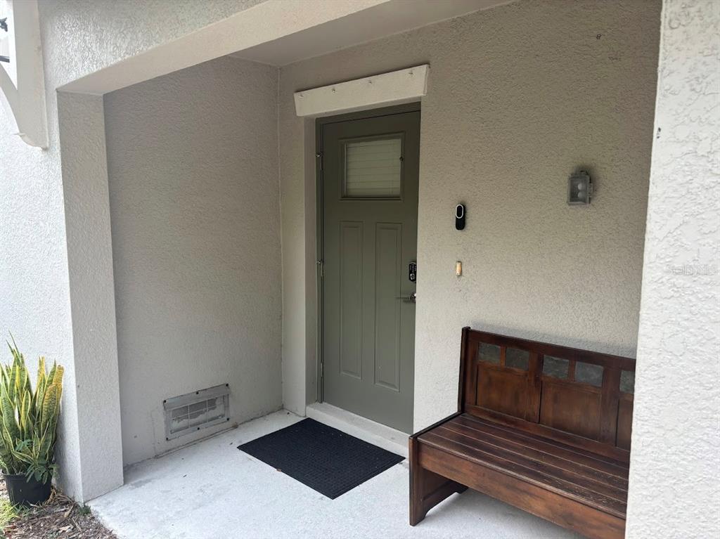 An exterior view of a covered entryway featuring a green door, bench, and potted plant — 870 TENNYSON MILL CIRCLE, TAMPA, FL