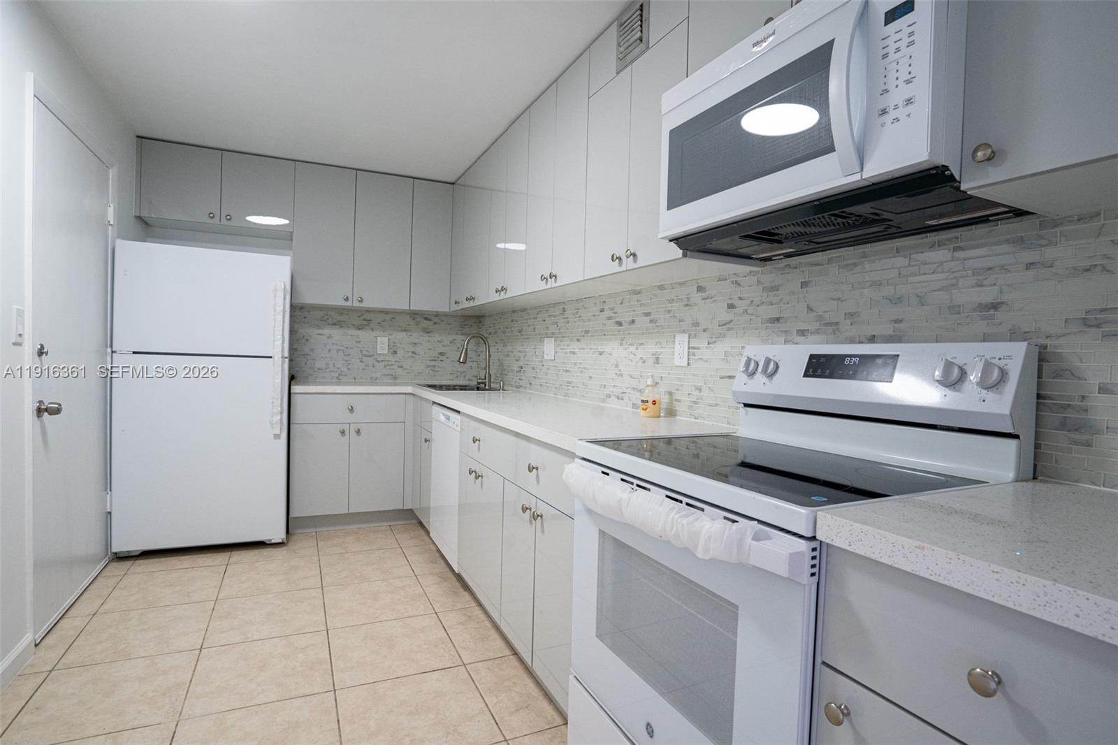 A kitchen features white appliances, light gray cabinetry, quartz countertops, and a tiled backsplash — 1849 S Ocean Dr # 1509, Hallandale Beach FL 33009, HALLANDALE BEACH, FL