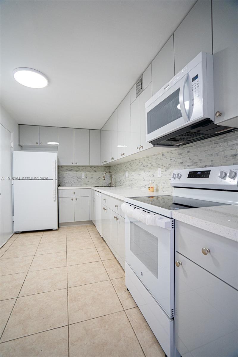 A galley-style kitchen features white appliances, light gray cabinetry, and a tiled backsplash — 1849 S Ocean Dr # 1509, Hallandale Beach FL 33009, HALLANDALE BEACH, FL
